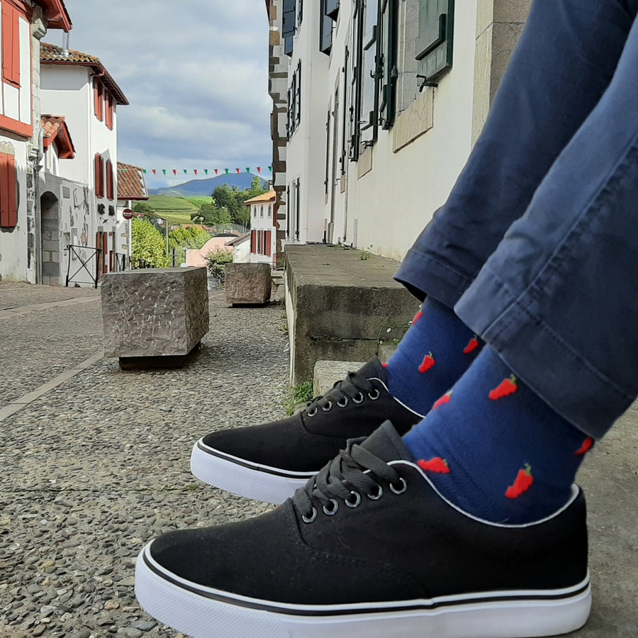 chaussettes Piment d'Espelette portées par modèle devant maisons basques et montagnes